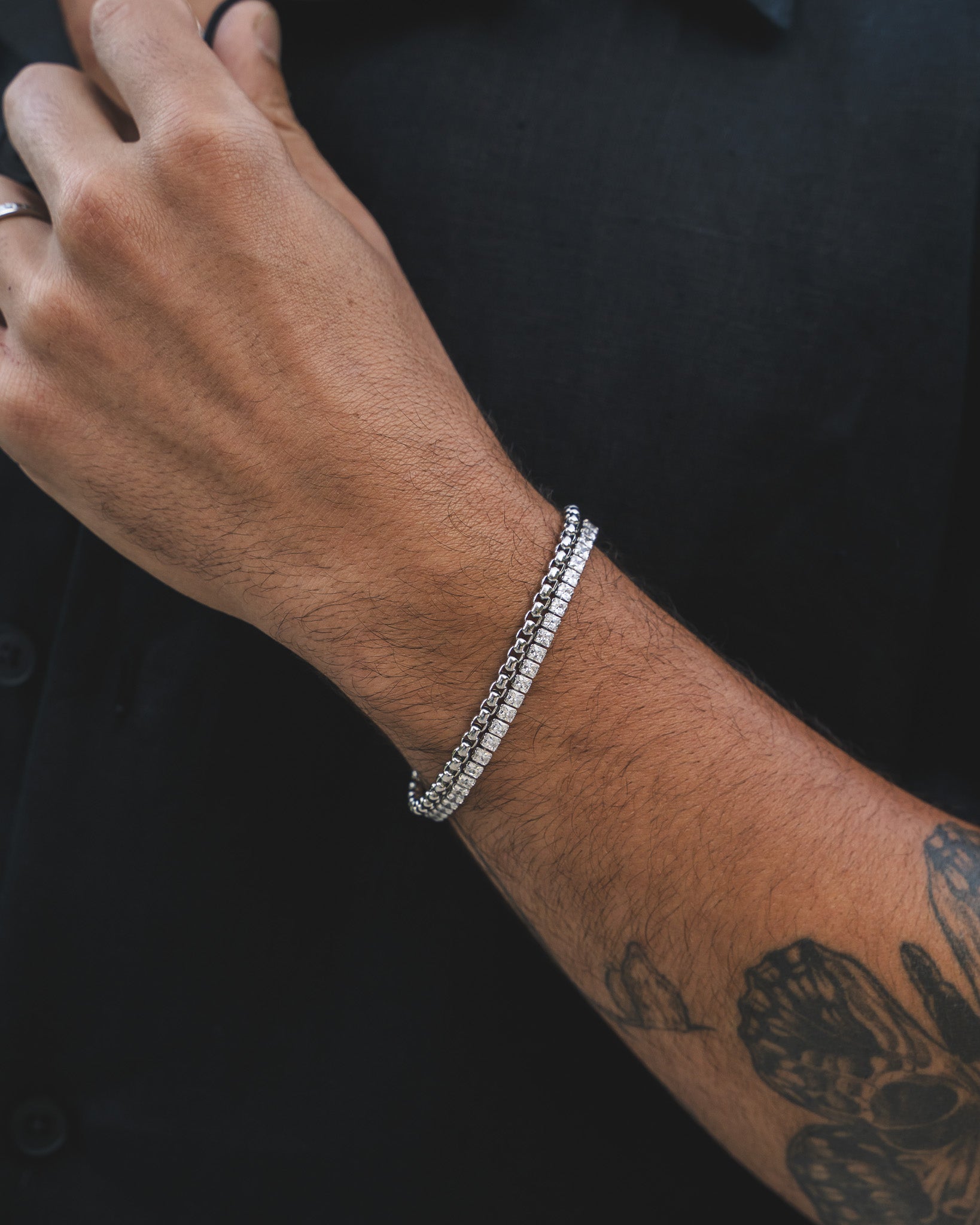 Close up of a man's wrist wearing a NOIR silver bracelet with a chunky chain against a dark shirt.