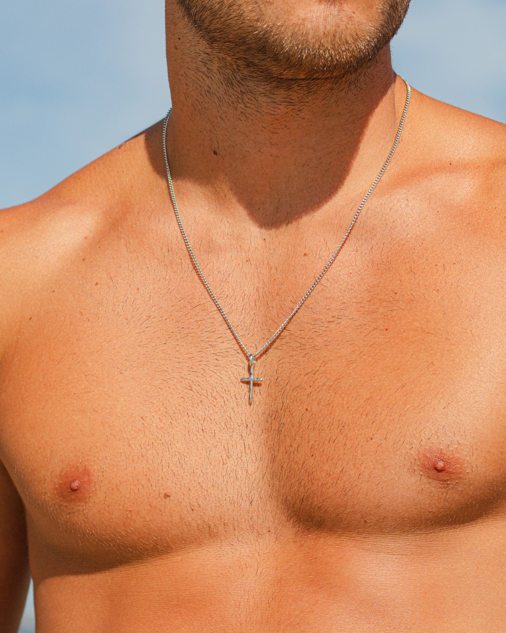 Close up of a silver chain necklace around a man’s neck against a blue sky.