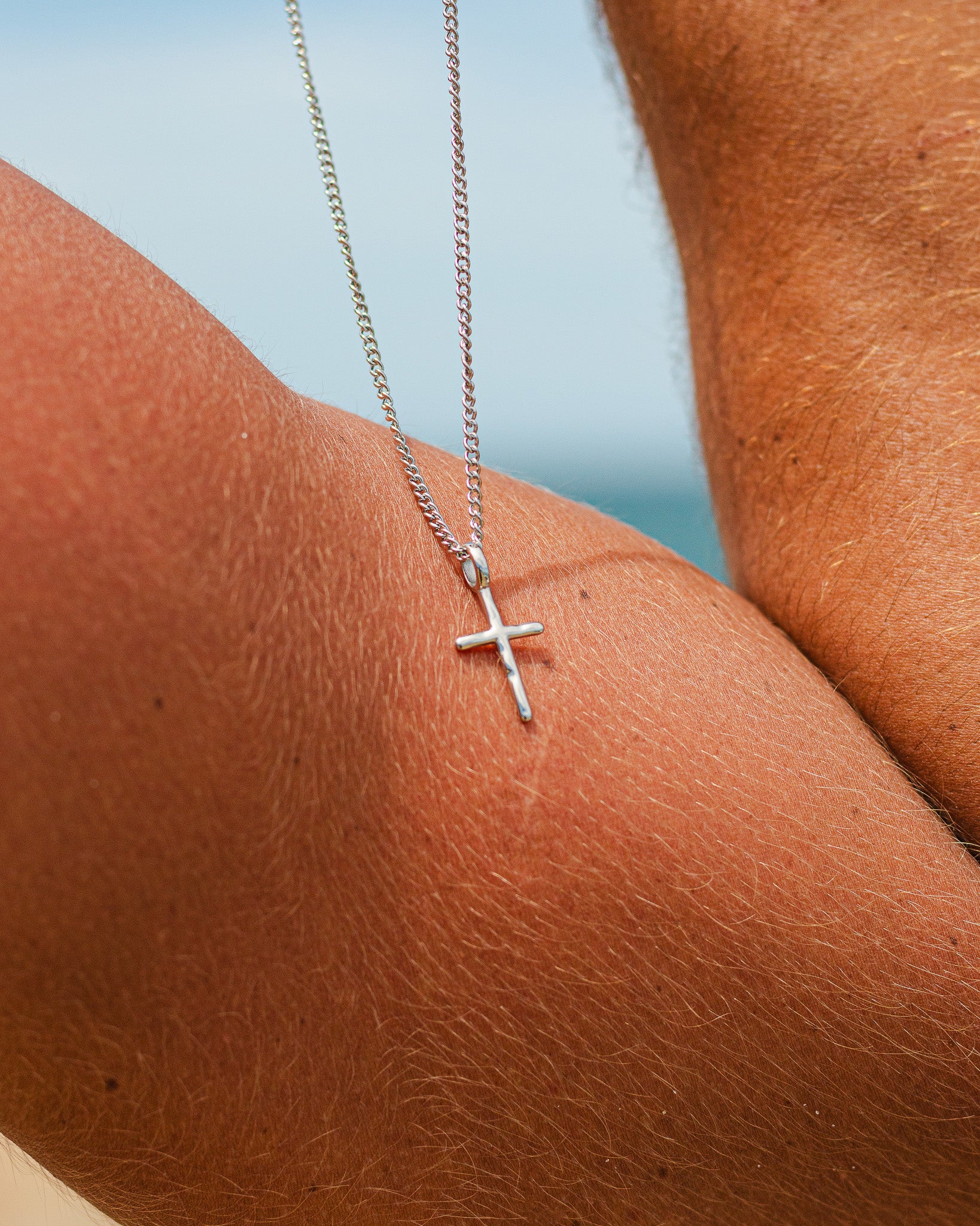 Silver chain necklace with cross pendant resting on a sunlit chest.