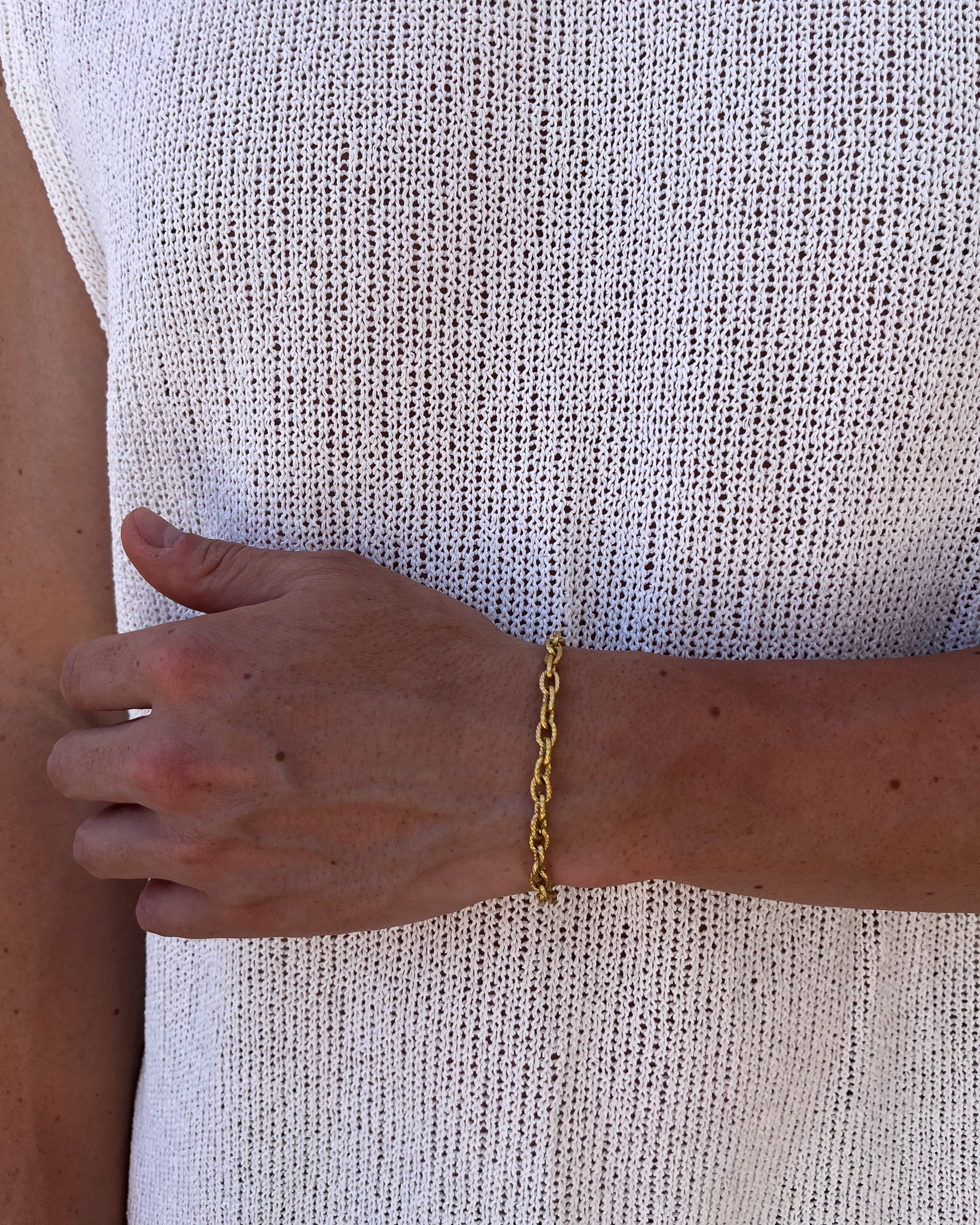 Wrist shot of a gold Saona bracelet on a forearm against a white knit top