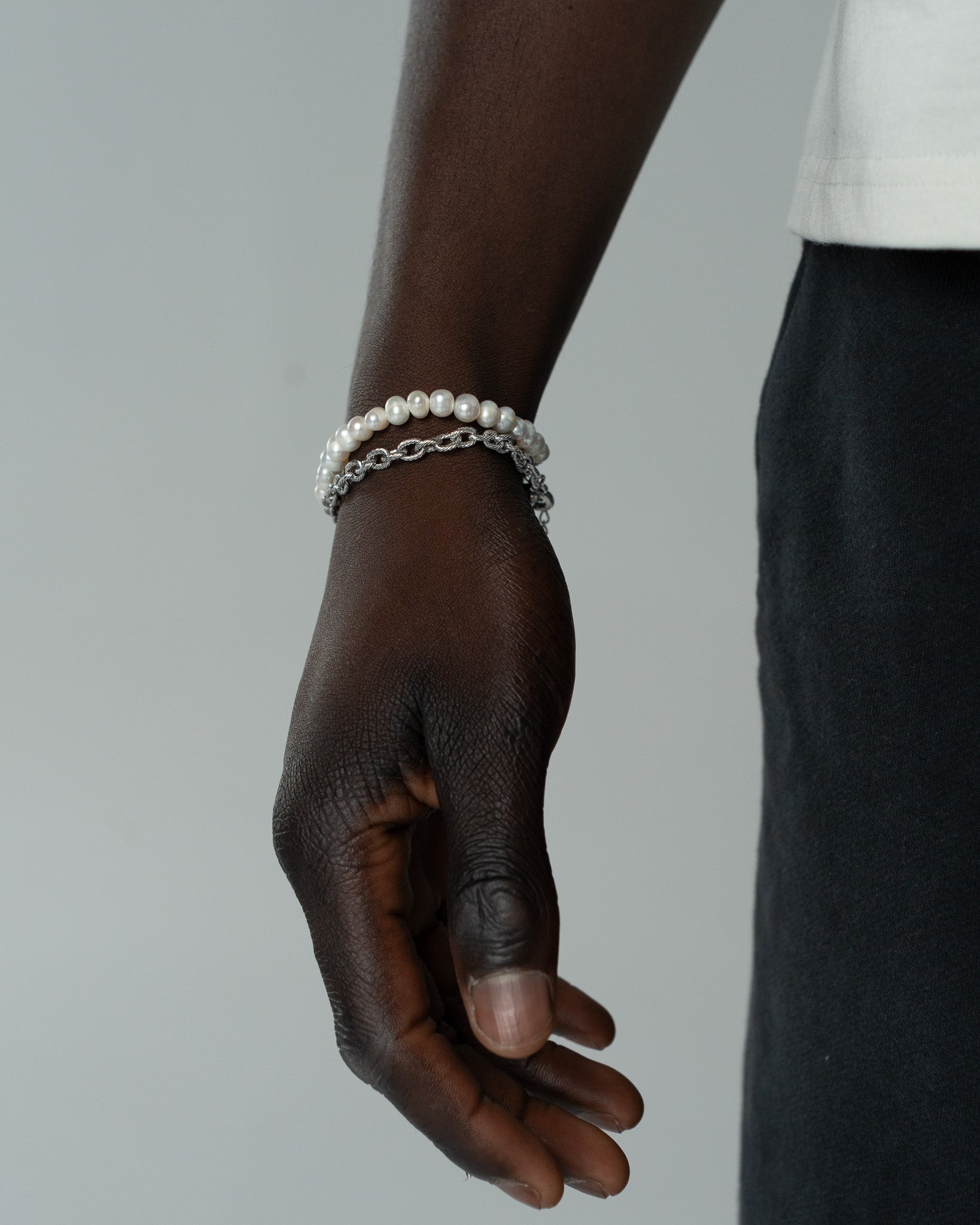 Pearl bracelet stacked with a silver chain bracelet on the model's wrist.