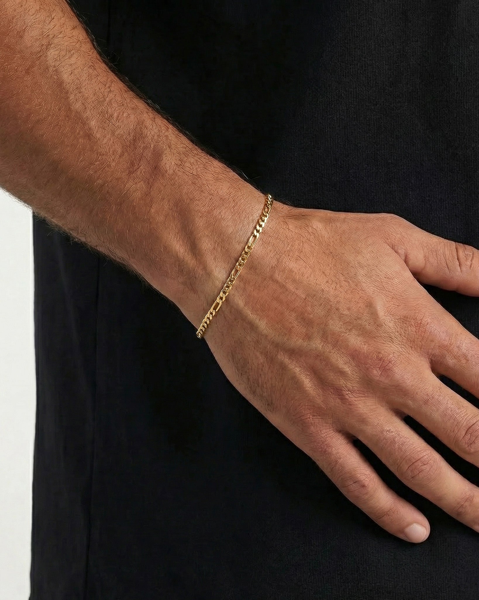 Amalfi Gold bracelet worn on a man’s wrist with a tiny red gemstone charm against a black shirt