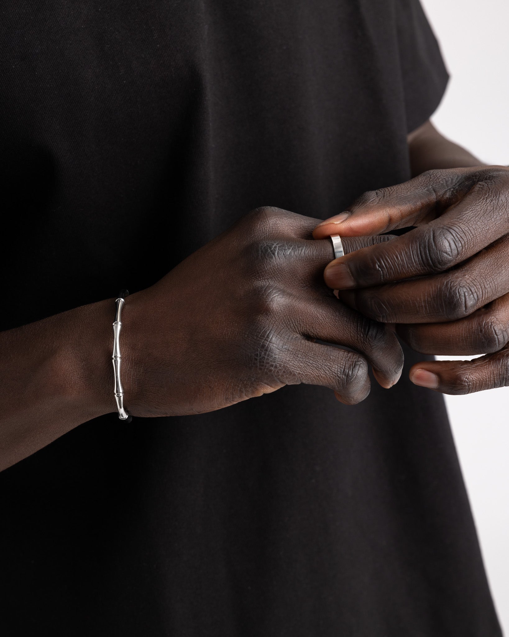 Close up of a dark skinned hand wearing a slim silver ring with a bracelet visible on the wrist