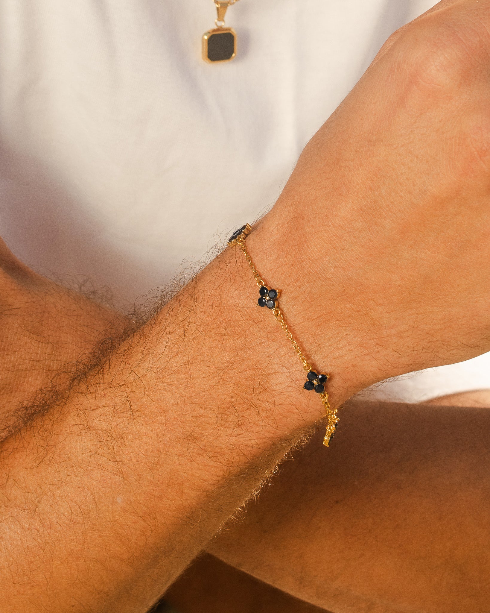 Pulsera dorada Clover con charm de flor negra de cuatro pétalos en la muñeca