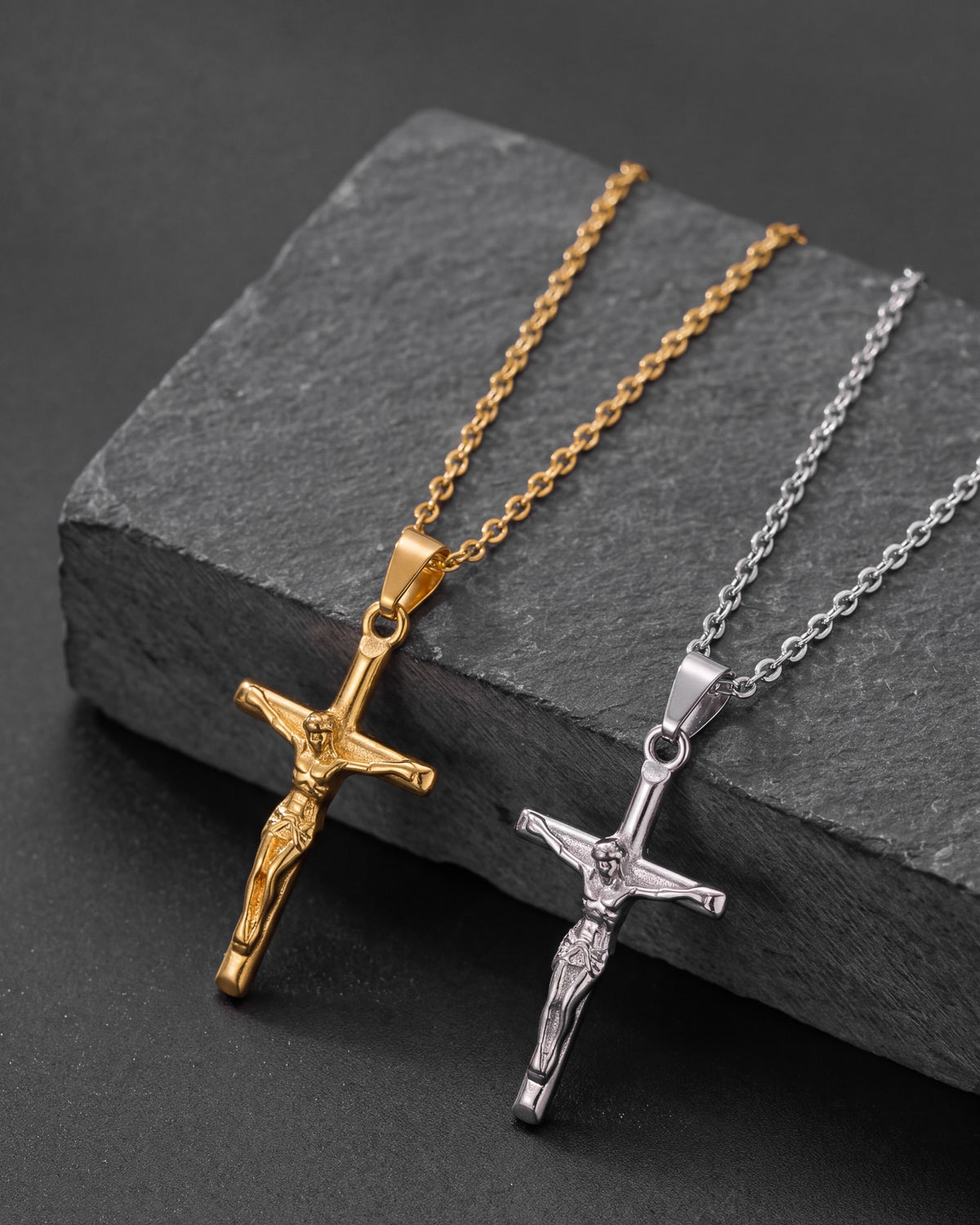 Gold and silver crucifix pendant necklaces with matching chains shown on a textured dark background.