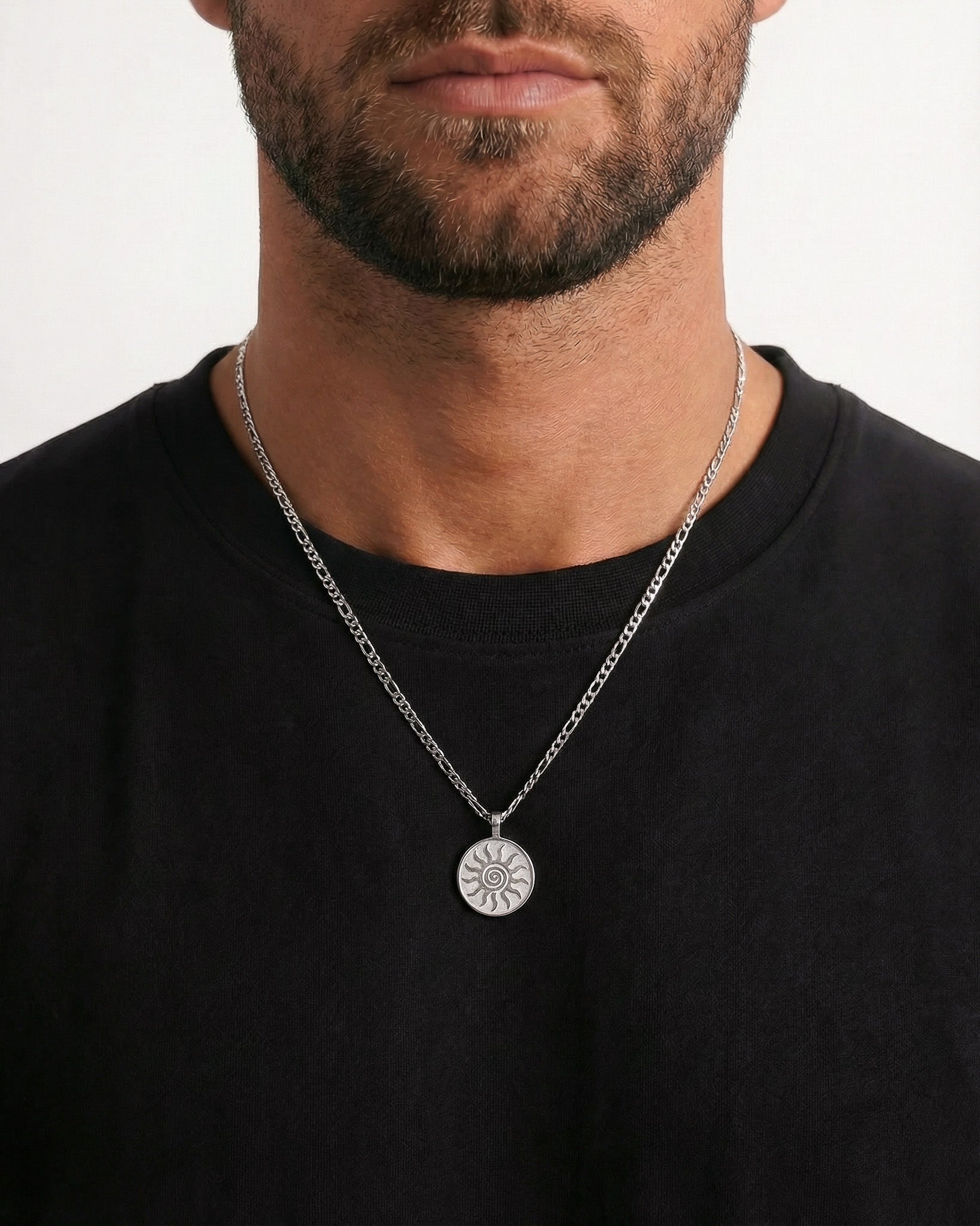 Close up of a man wearing a silver energy necklace with a round sunburst pendant.