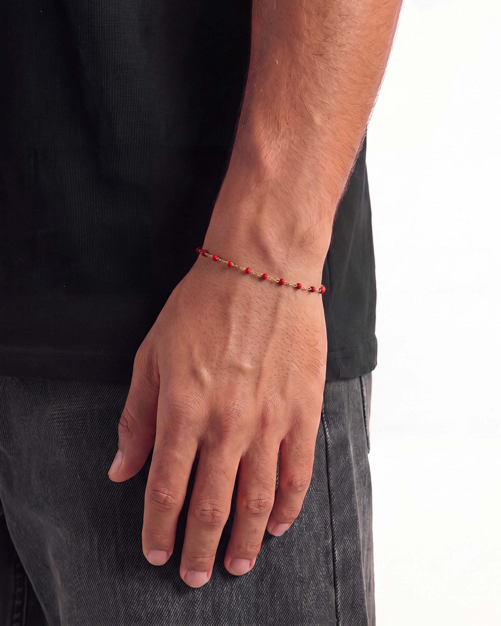 Vista lateral de una pulsera dorada con cuentas rojas en la muñeca