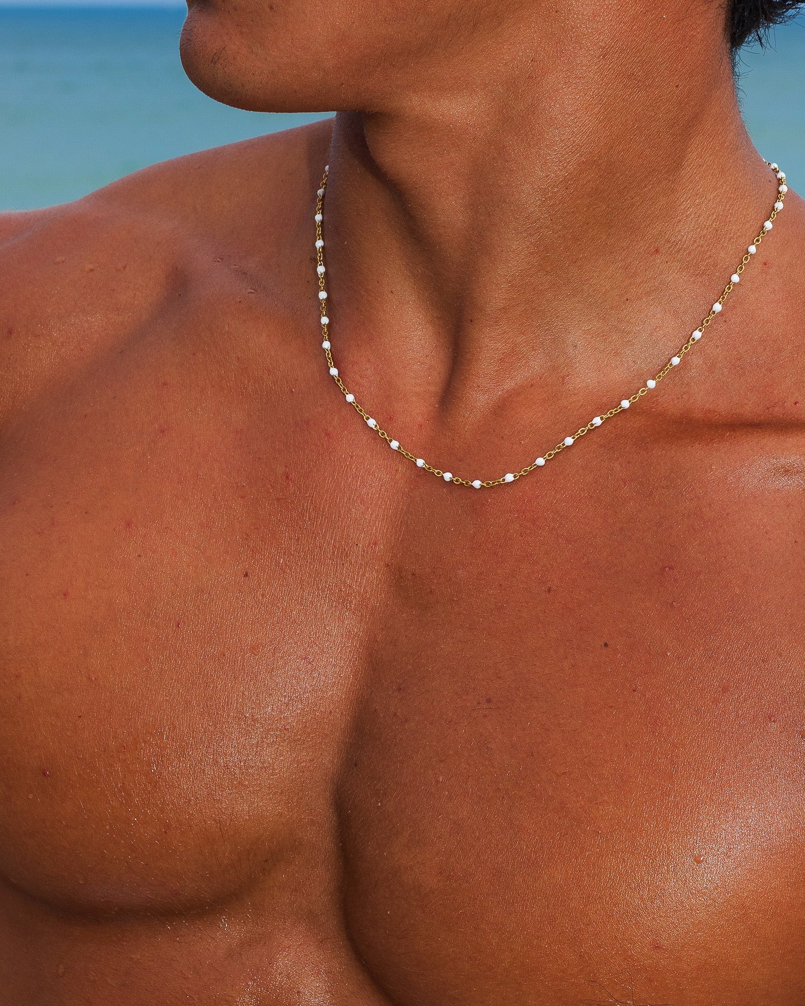 Collar de cadena de oro con cuentas blancas pequeñas sobre un pecho bronceado