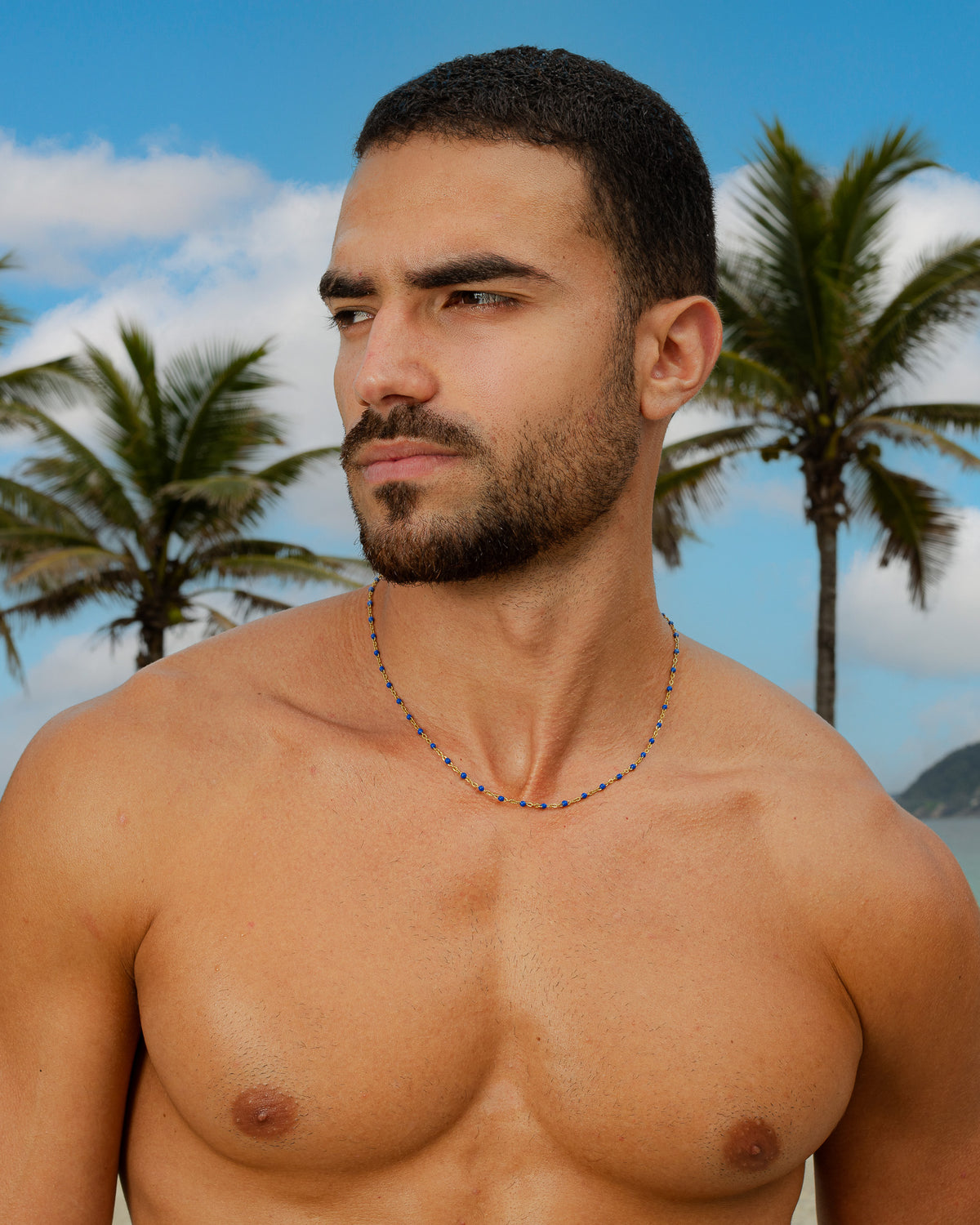 Hombre con una cadena de oro con cuentas azules sobre un fondo de playa tropical