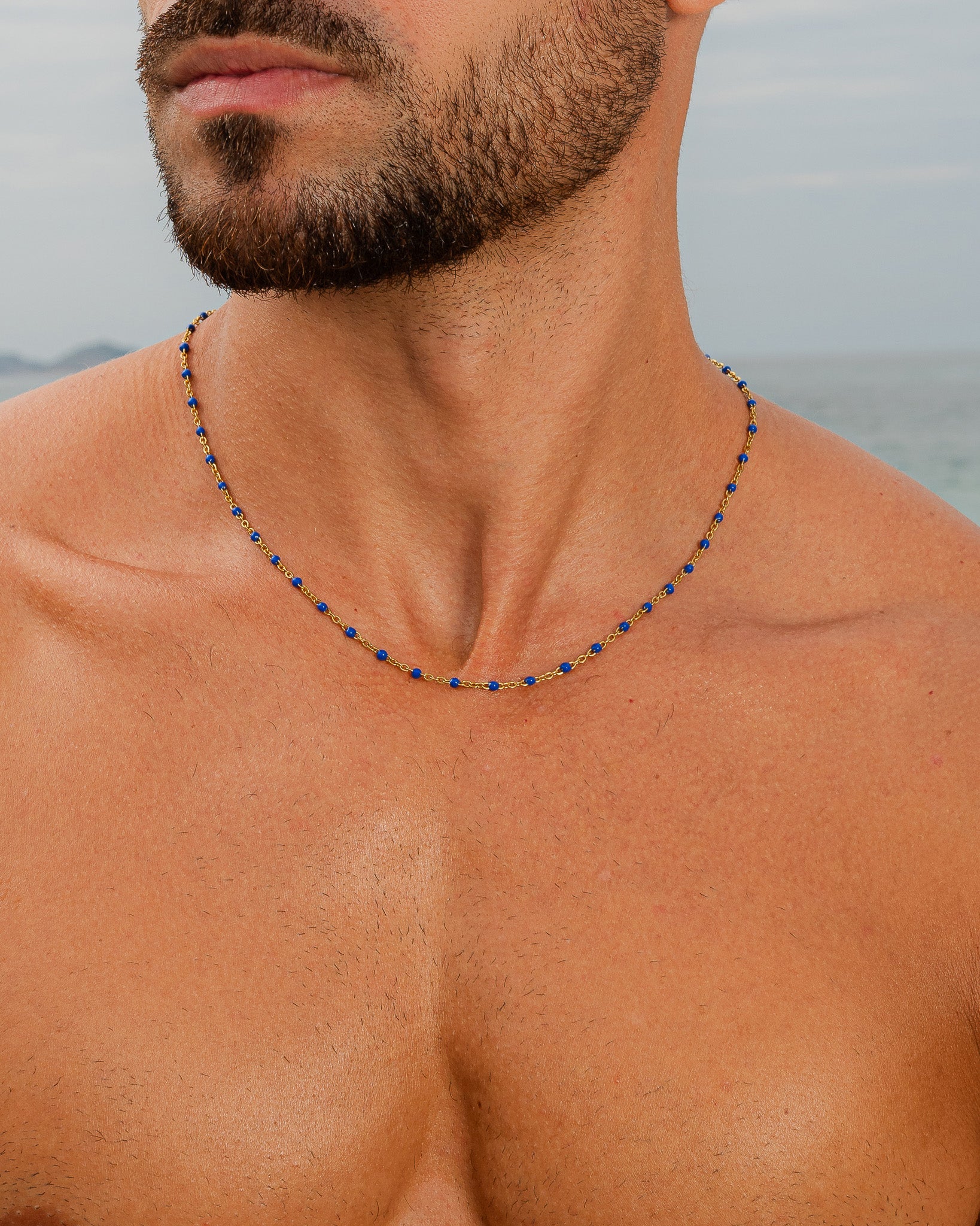 Cadena de oro con cuentas azules en el cuello de un hombre en la playa.
