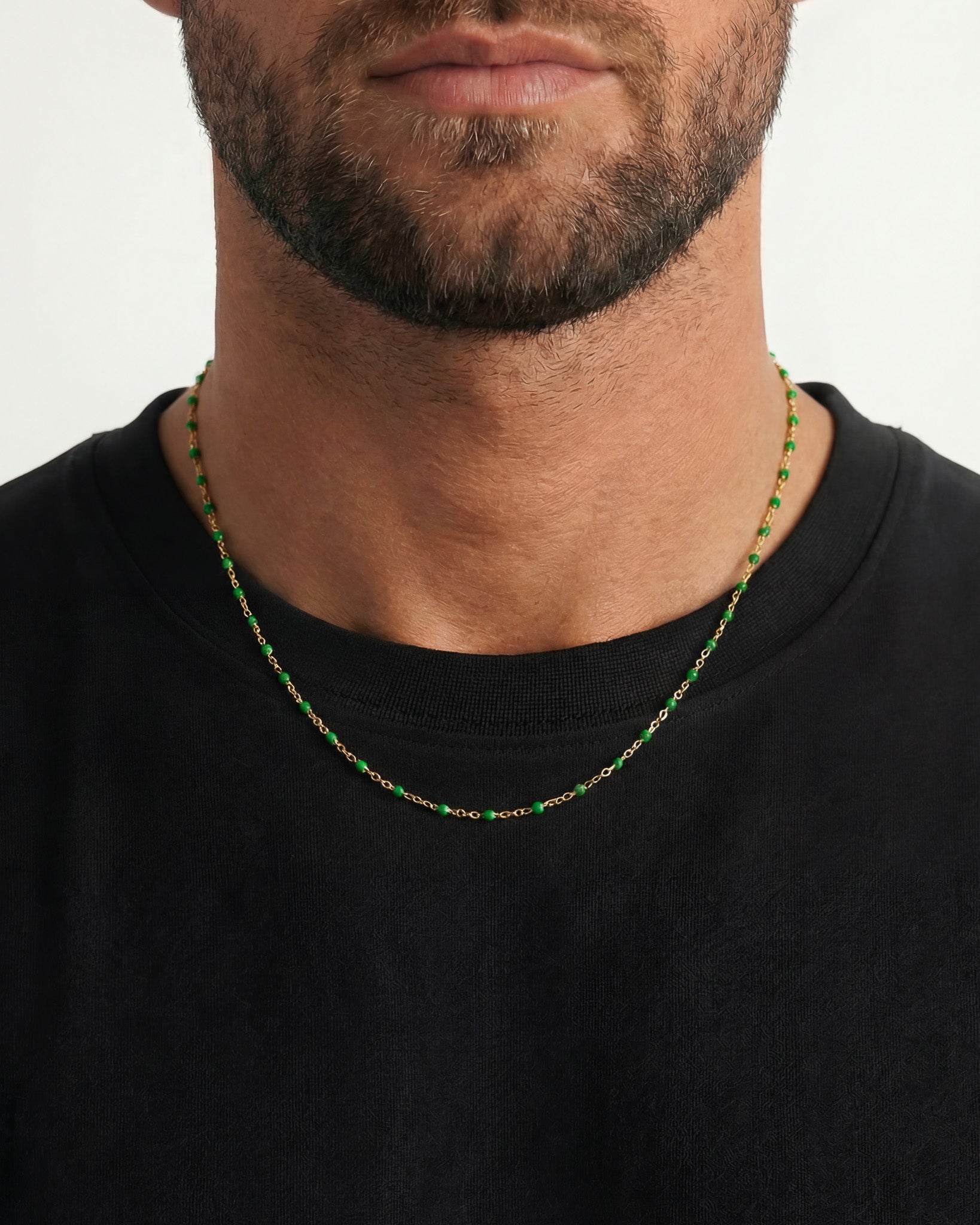 Close up of a neck wearing two gold chains with small green beads, creating a layered look.