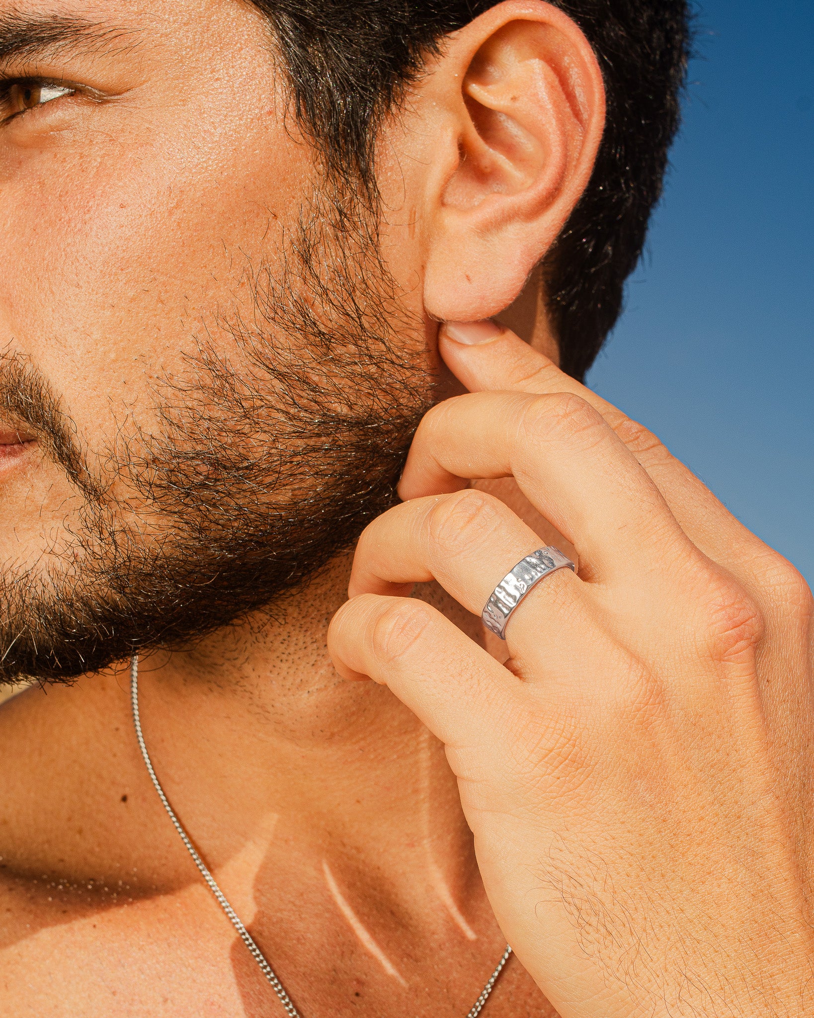 Perfil de un hombre con el anillo plateado martillado de 6 mm en el dedo y collar de cadena plateada visible en el cuello.