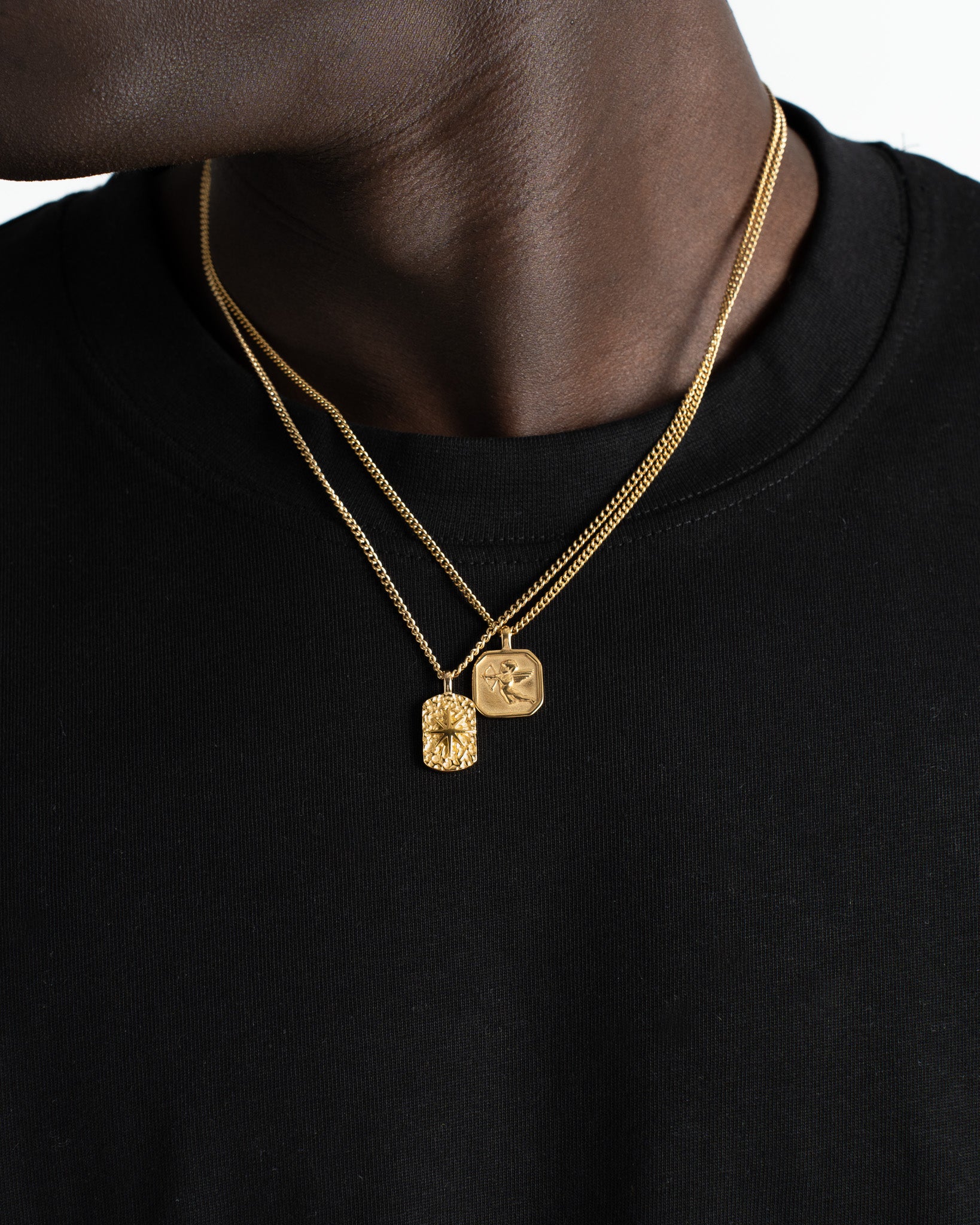 Layered gold chains with two square pendants resting on a model's bare chest