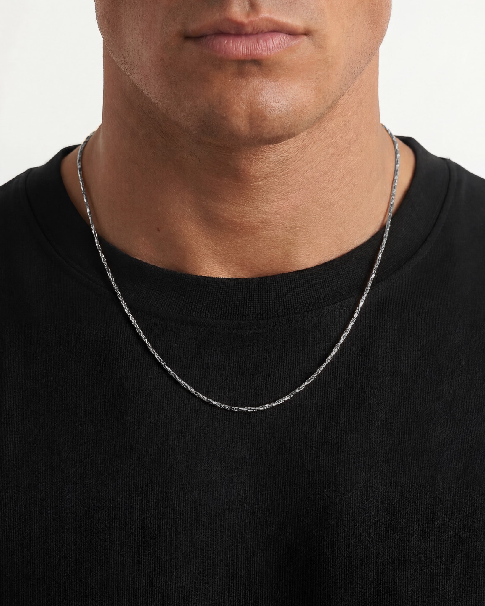Close up of a minimal silver chain worn on a model's neck over a black shirt