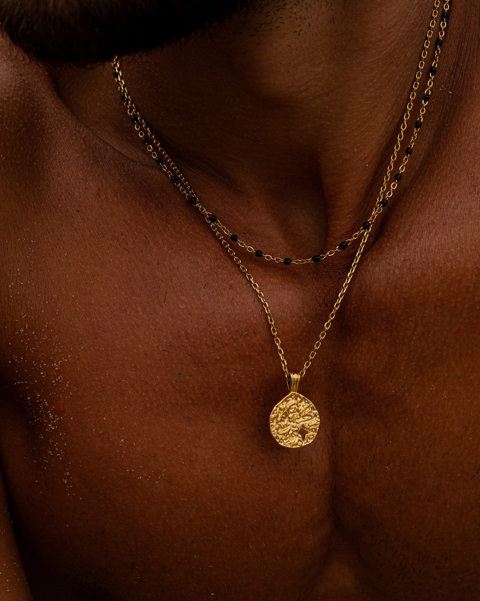 Primer plano de un collar de cadena de oro con detalles de cuentas negras en el cuello del modelo
