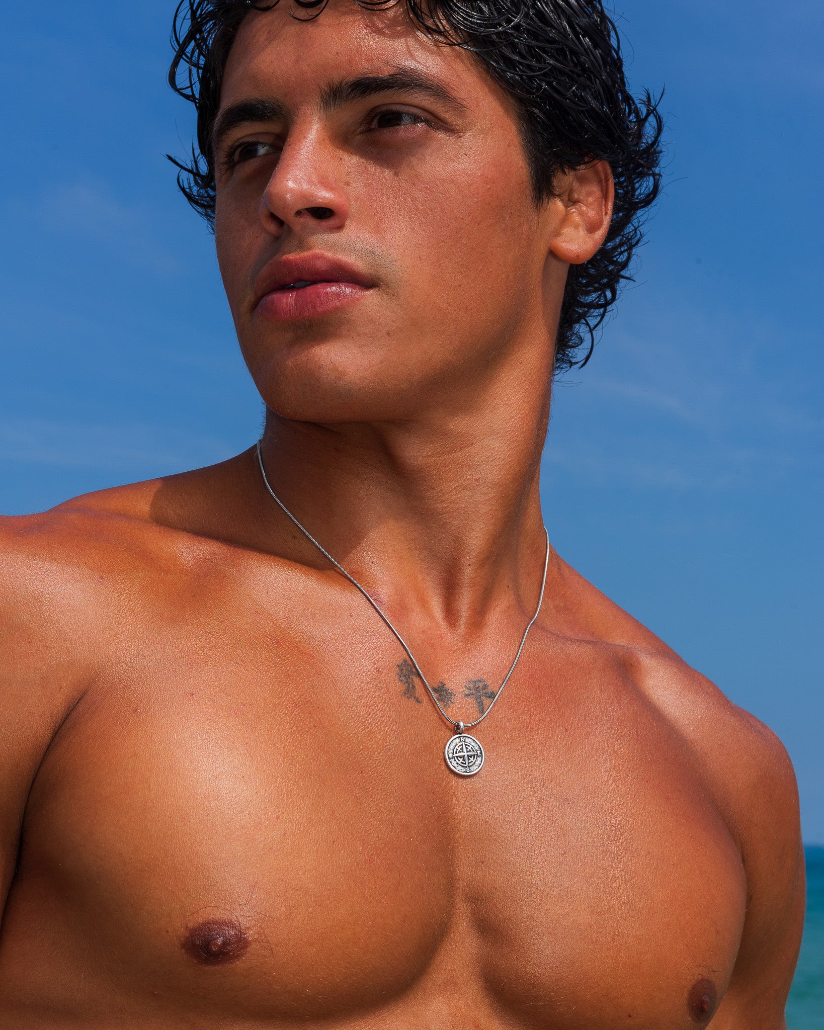 Collar MOJAVE de plata con colgante de medallón redondo sobre un pecho tatuado en la playa