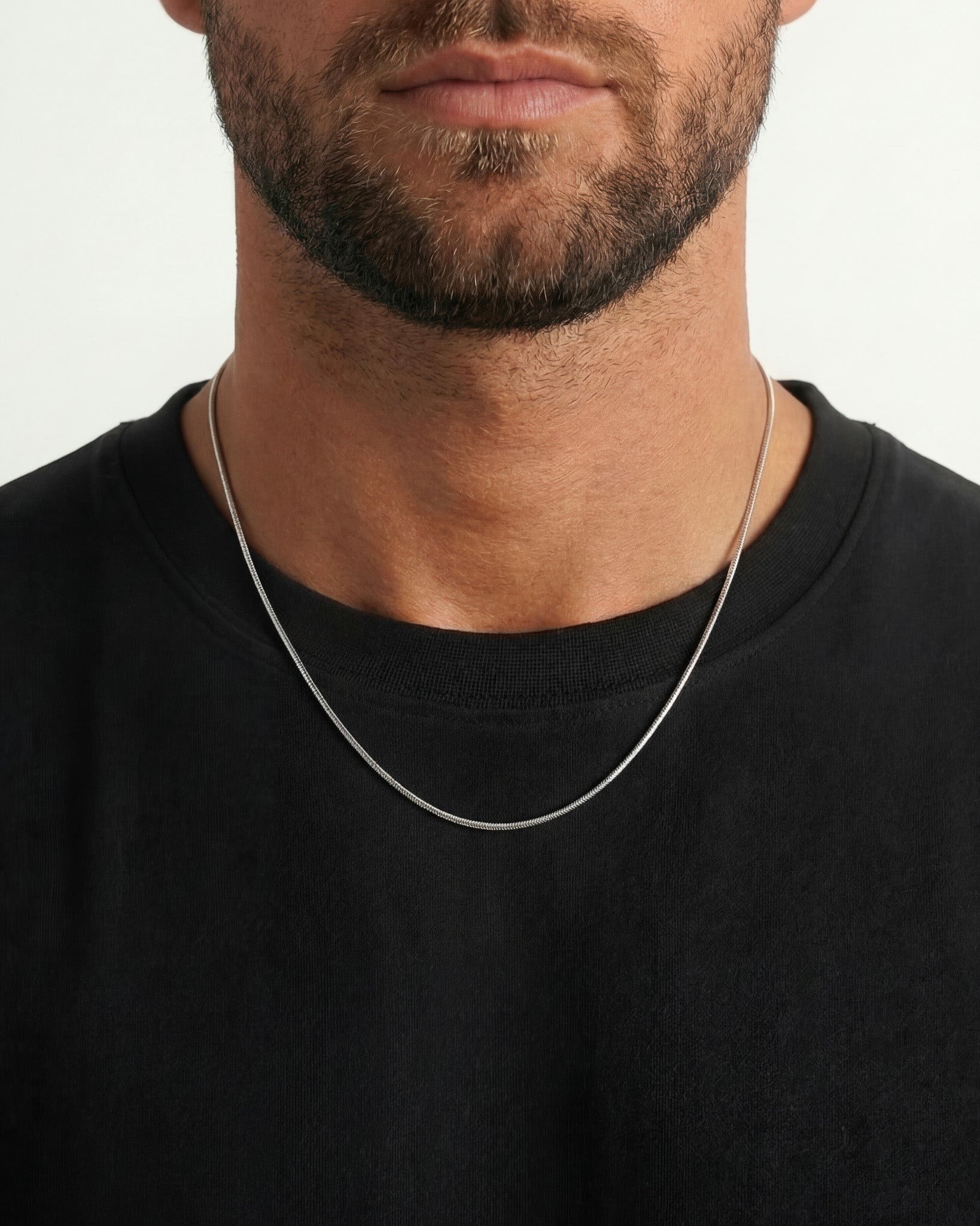 Close up of a man wearing two silver chain necklaces around the neck with a pendant