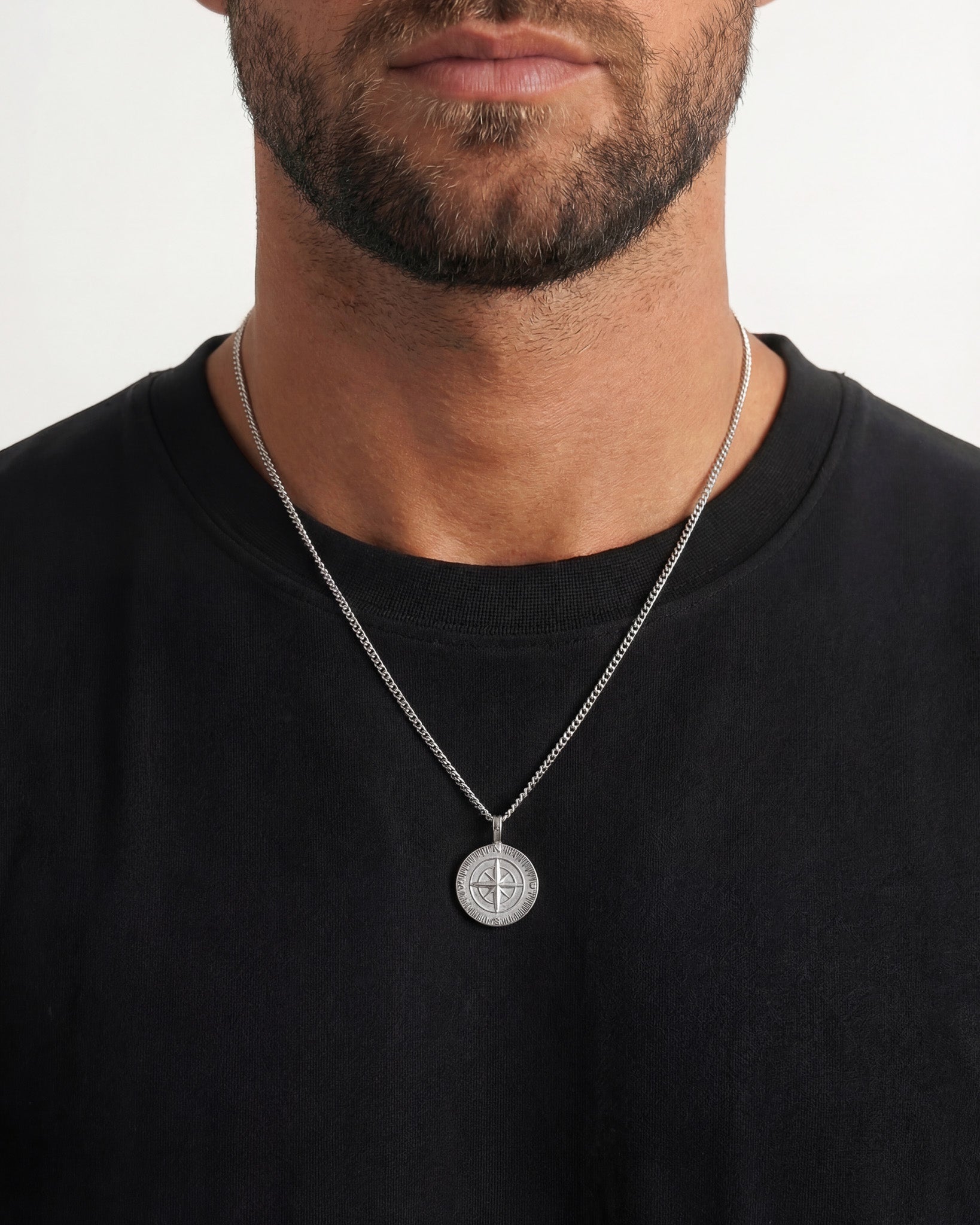Man wearing a silver compass pendant necklace over a black shirt