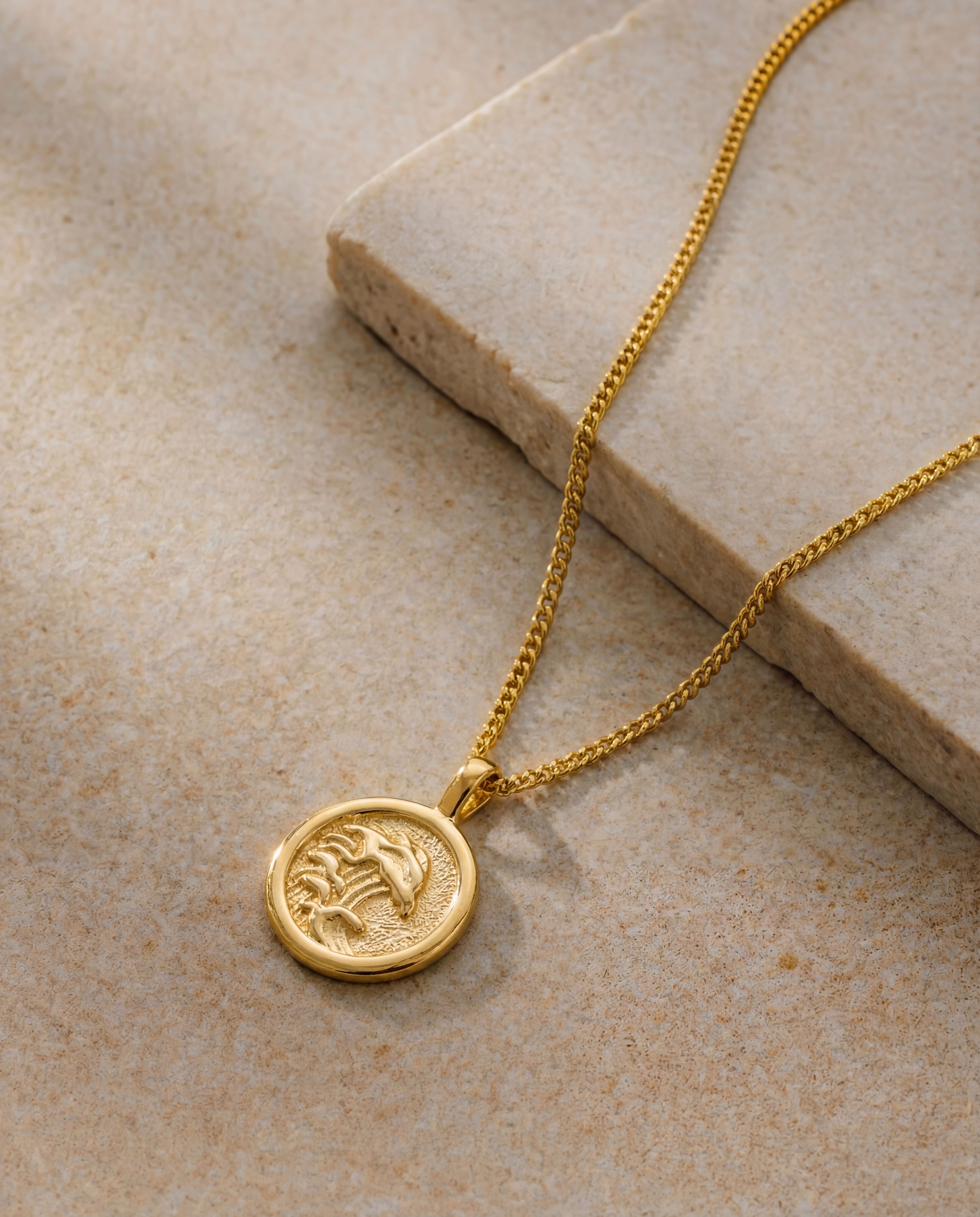 Close up of a gold palm tree pendant on a textured stone backdrop with chain