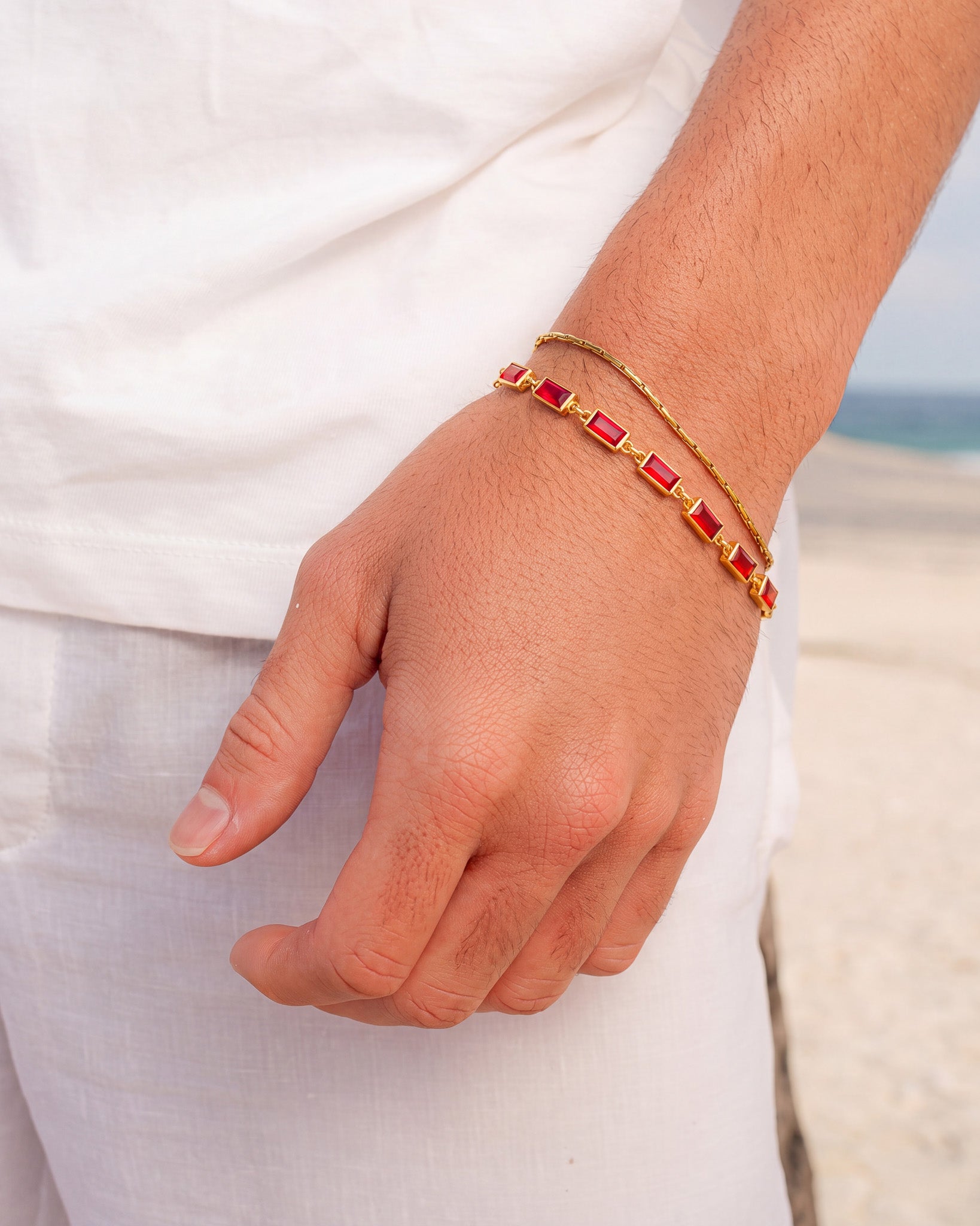 Pulsera OMEN de oro con gemas rectangulares rojas en la muñeca, con el cierre a la vista