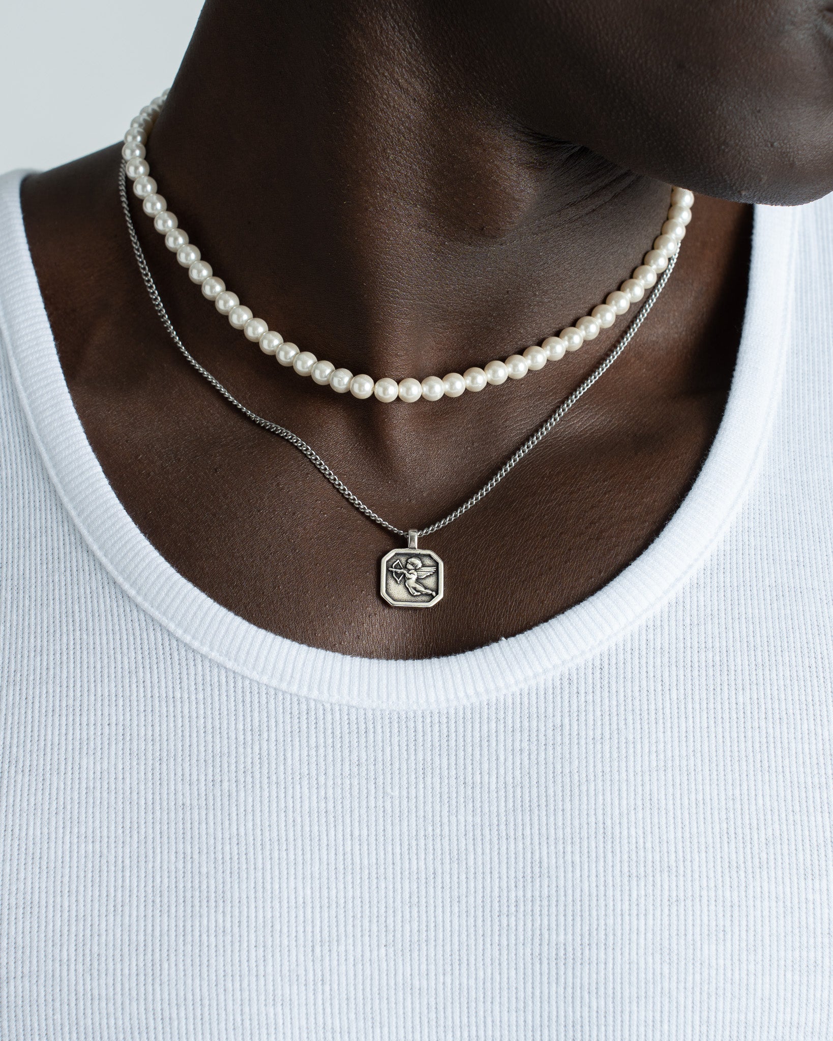 Two-layer Bellagio Pearl Chain look with a pearl strand and a silver pendant necklace on a white top.