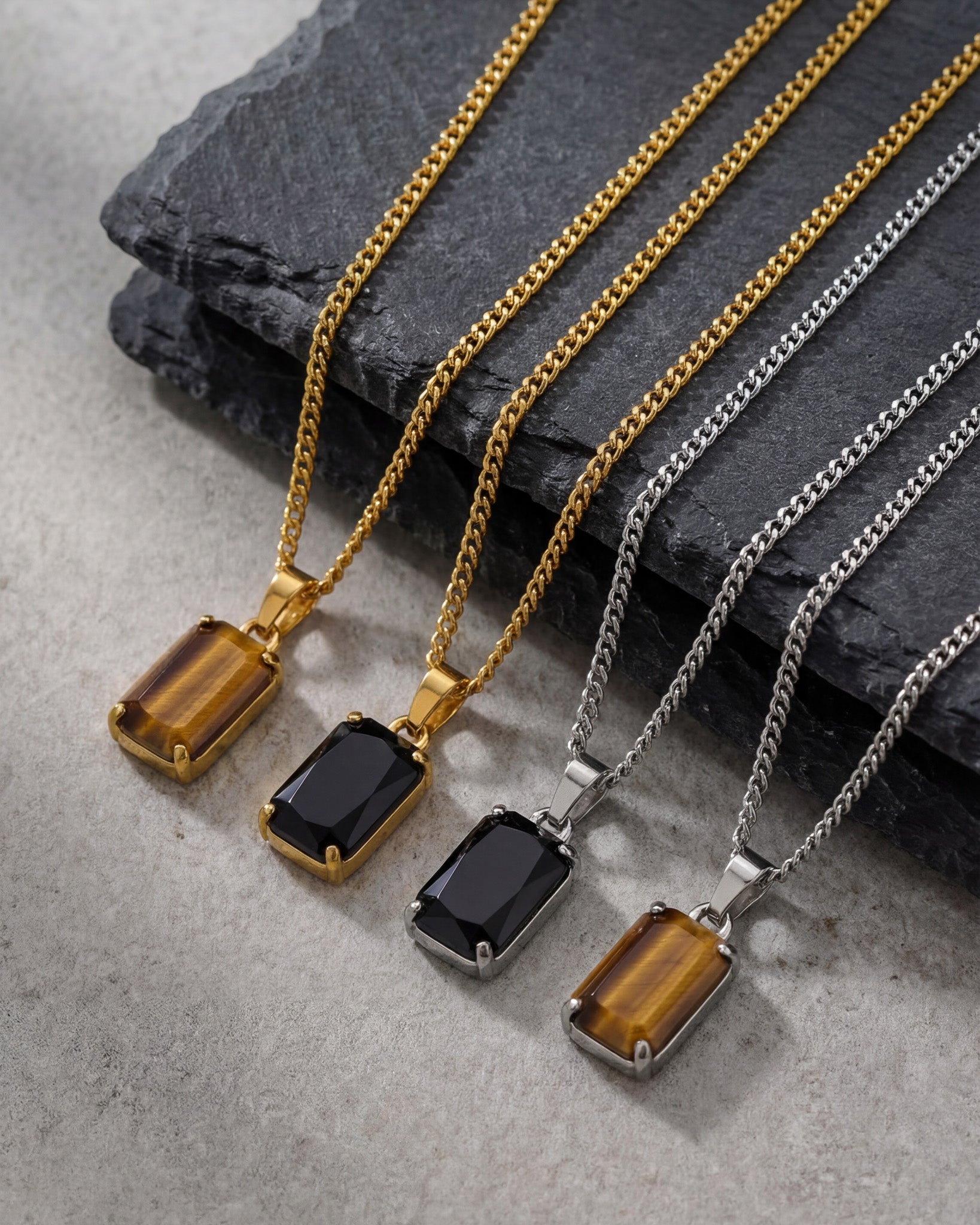 Gold and silver VOLT necklaces with rectangular gemstone pendants arranged on a dark slate surface